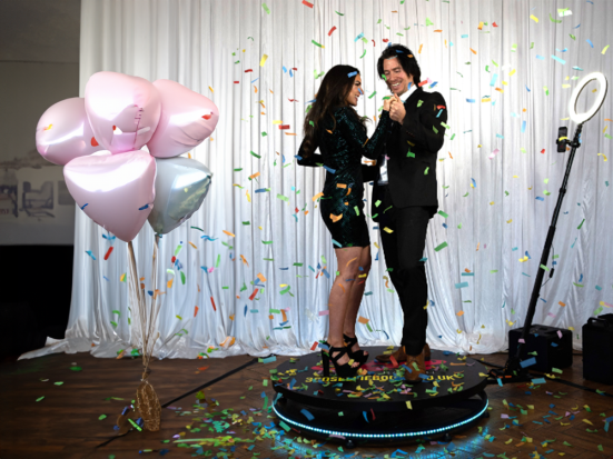 Couple on 360 photo booth with confetti and balloons