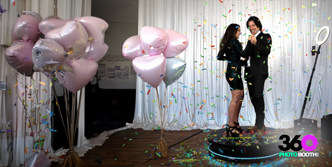 Couple posing on a rotating platform with balloons and confetti.
