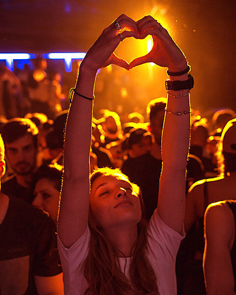 Crowd enjoying a lively event, person forming a heart shape with hands.