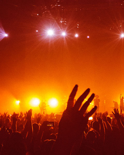 Audience with hands raised at an event under lights.