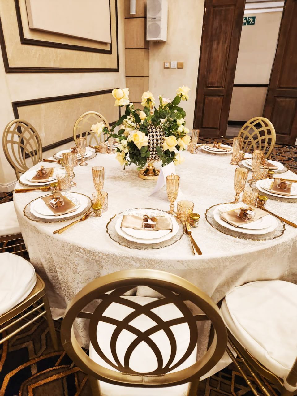 Elegantly set table with golden cutlery and yellow rose centerpiece.