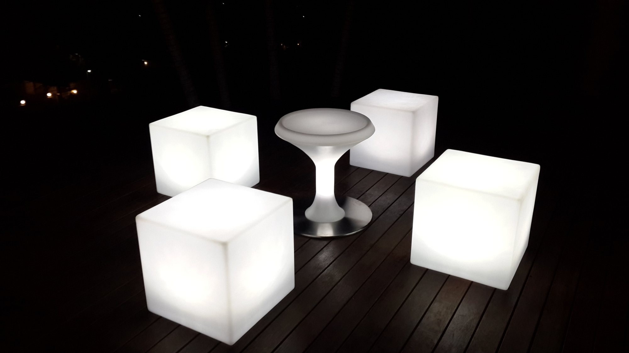 Four illuminated cubes and a round LED stool in a dark setting.