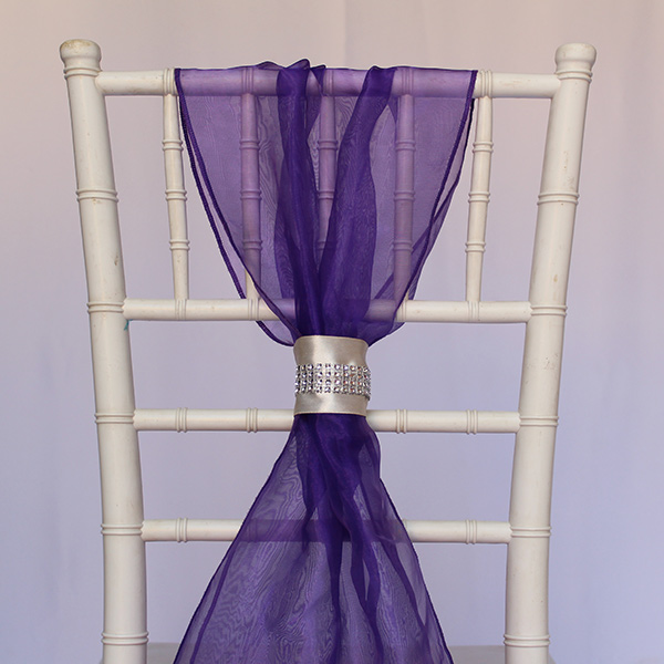 White chiavari chair with purple drape and rhinestone accent.
