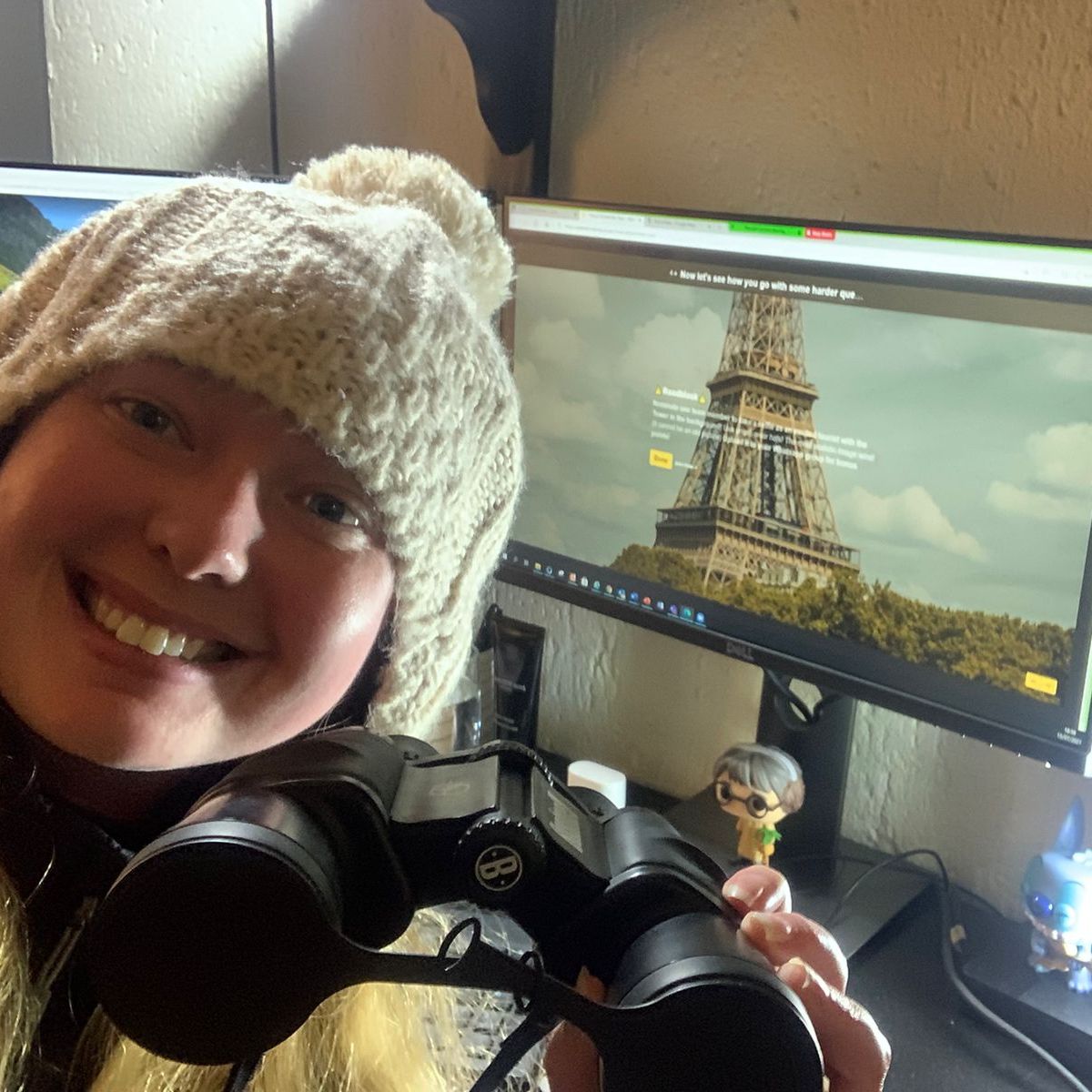 Person smiling with binoculars in front of a computer displaying a virtual experience.