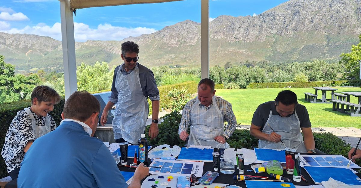 Group of people painting outdoors with mountains in the background.