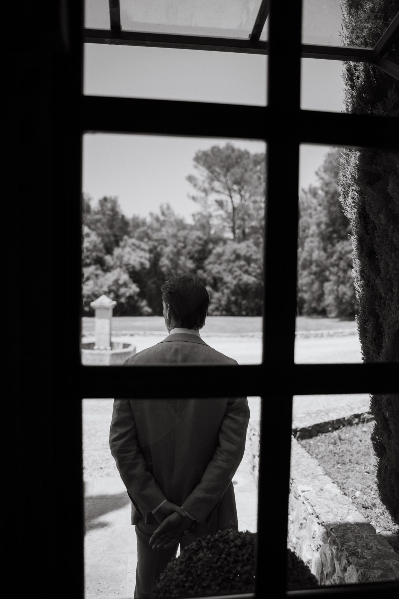 A man in a suit viewed through a window, standing outdoors.