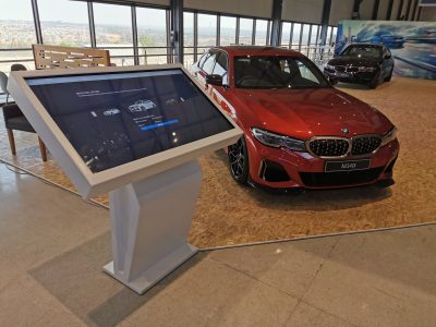 Touch screen kiosk beside a red BMW car