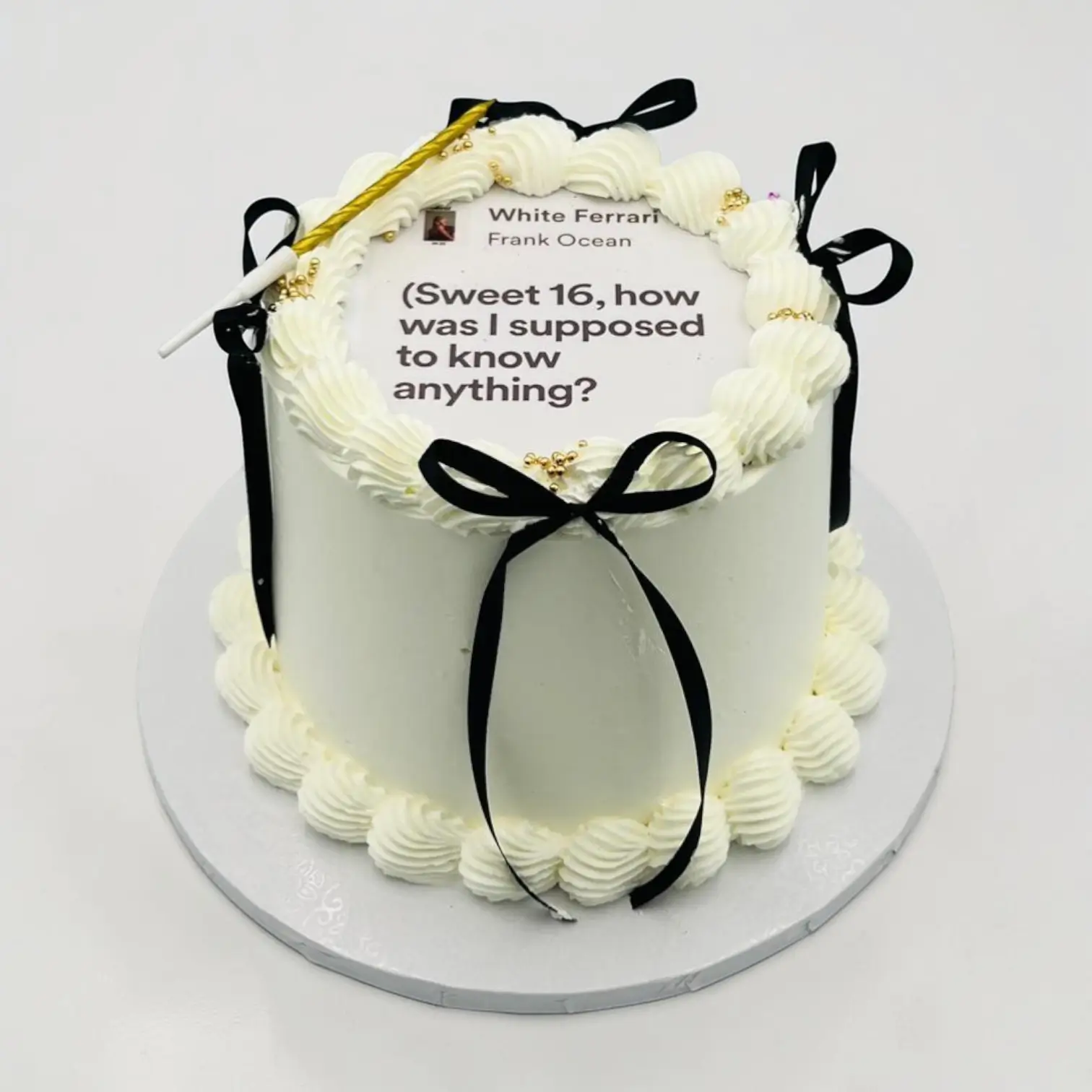 White cream cake with black ribbons and a lyric on top