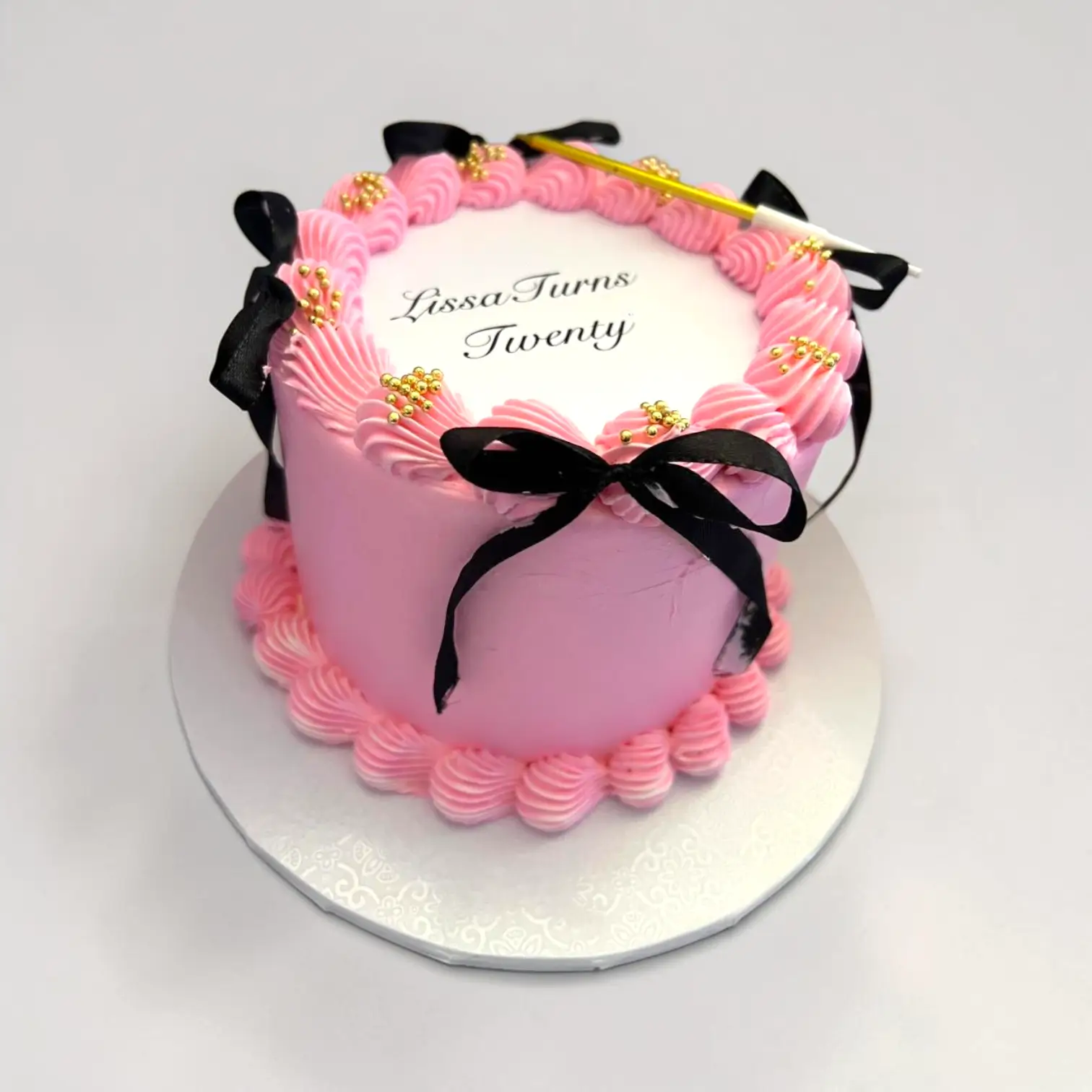 Pink birthday cake decorated with ribbons and gold accents.