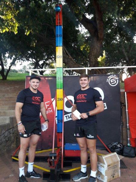 Two men beside a height measurement game at an event.