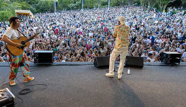 Musicians performing at a large outdoor concert with an audience.