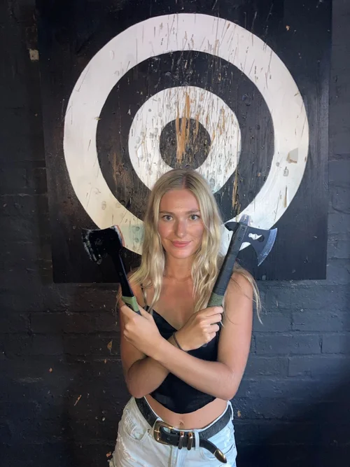 Participant posing with two axes in front of a bullseye target.