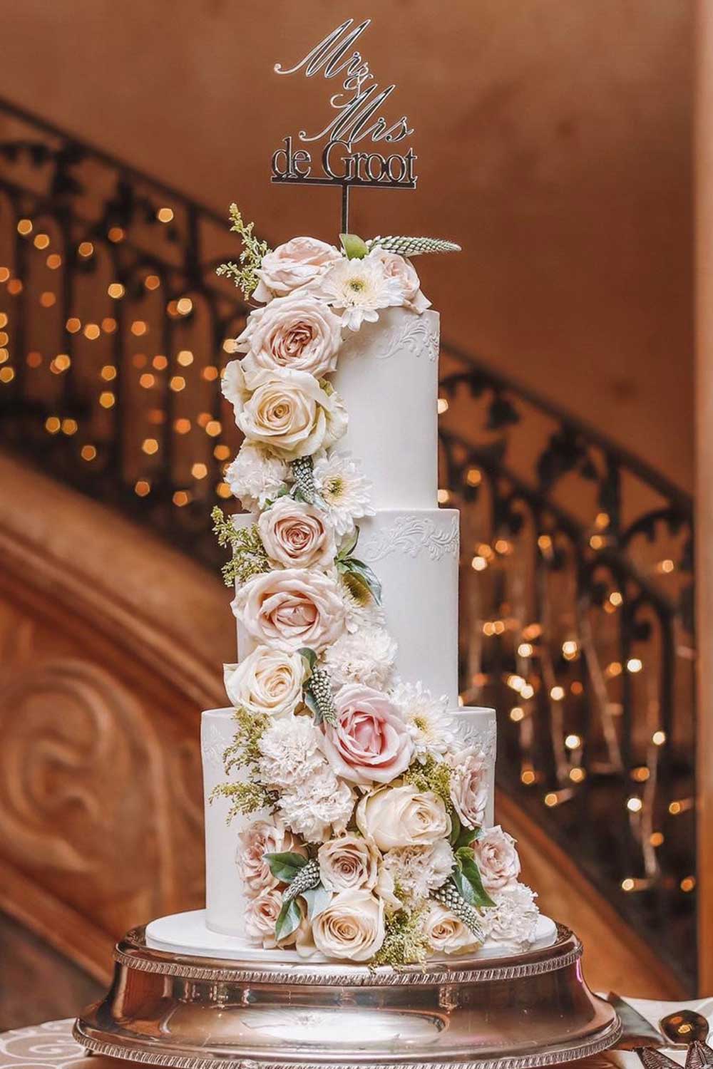 Three-tiered floral wedding cake with decorative flowers and a 'Mr & Mrs' topper