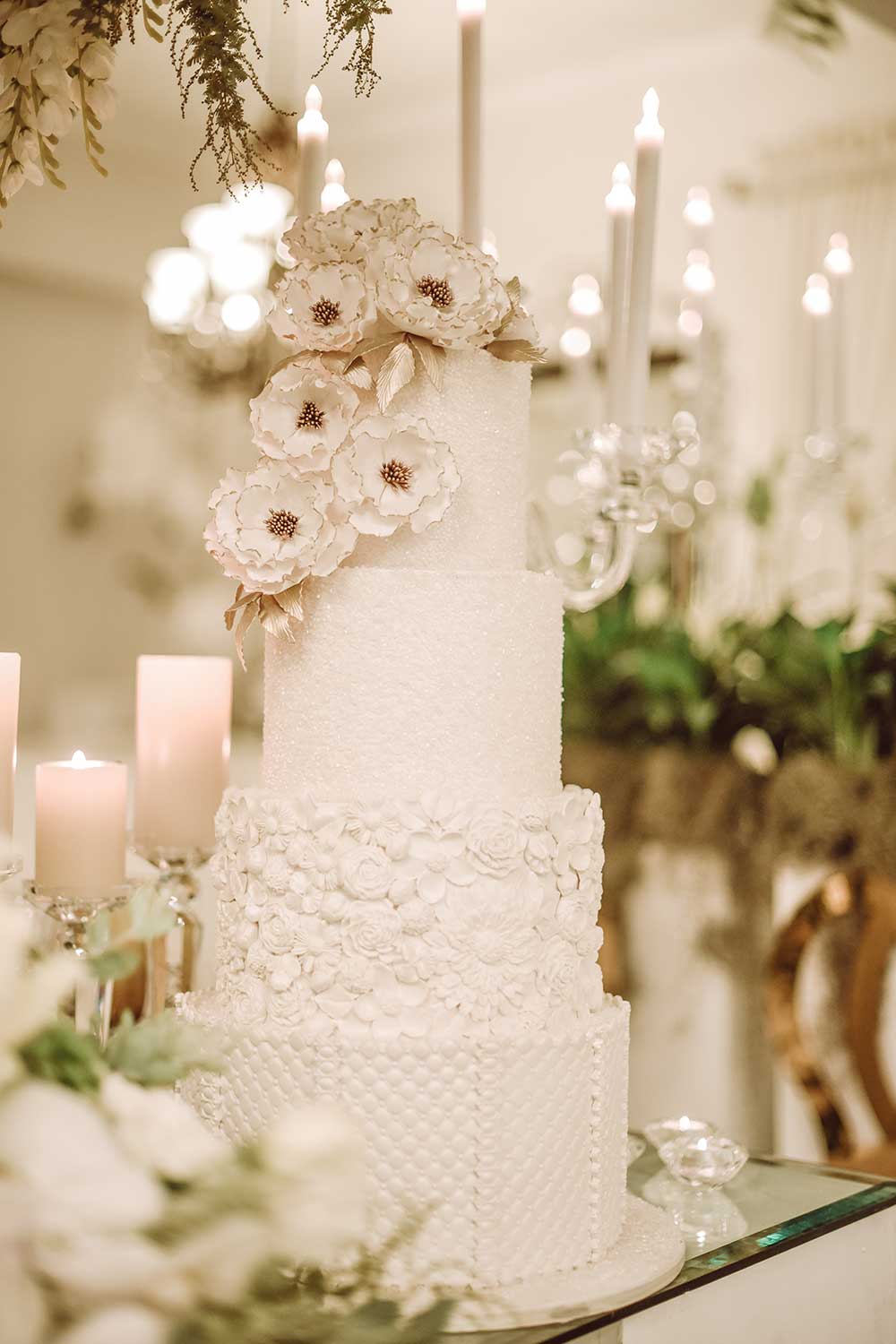 Three-tier white wedding cake with sugar flowers and candles
