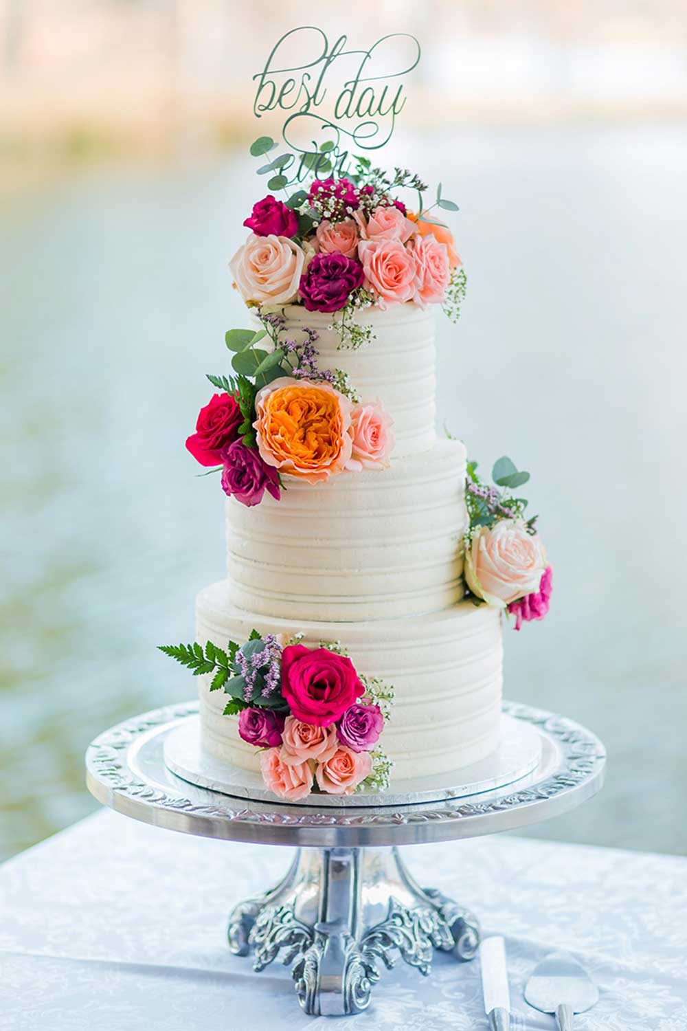 Three-tiered wedding cake with flowers and a 'Best Day' topper.