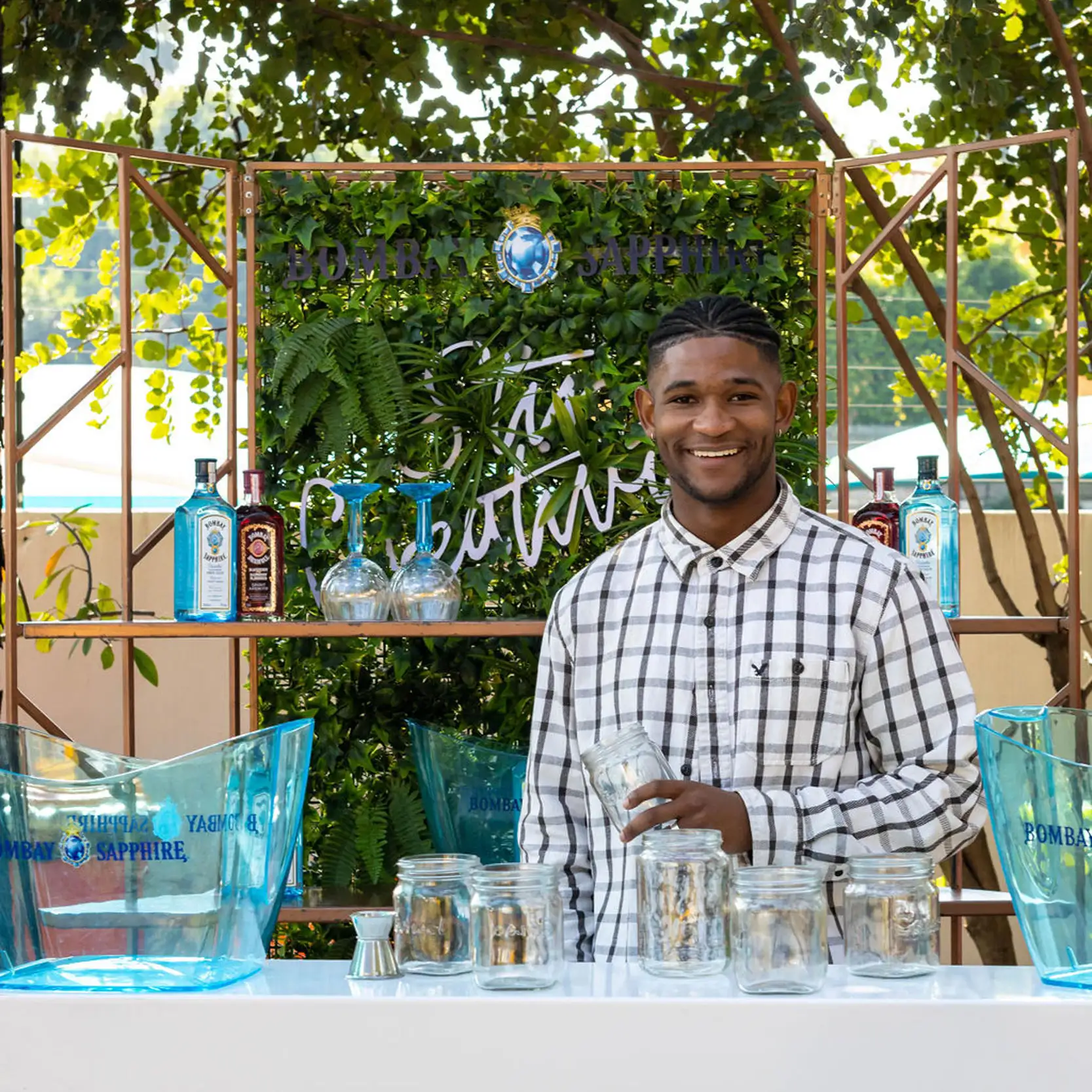 Bartender at a gin bar with greenery and gin bottles.