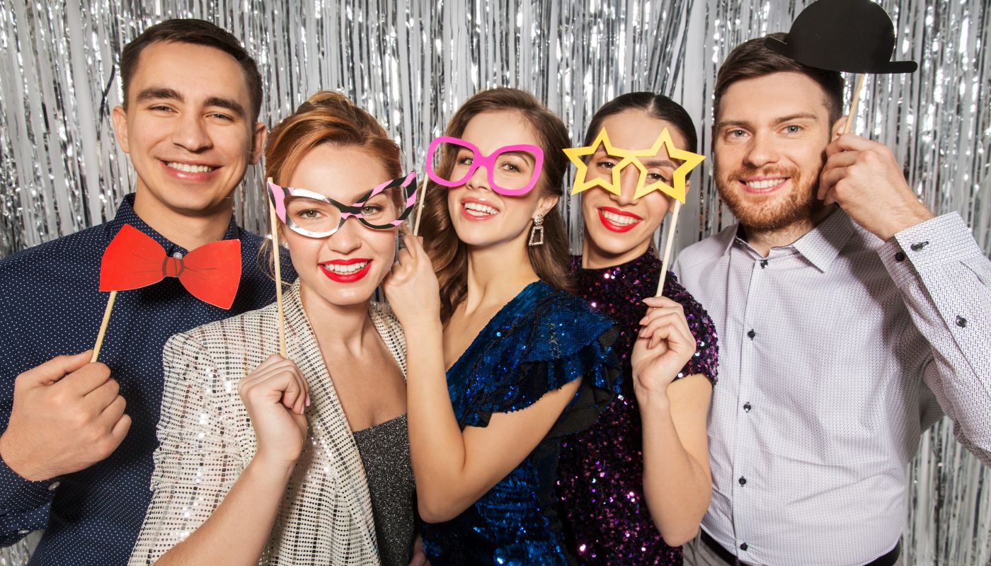 Five friends posing with props in front of a silver backdrop.
