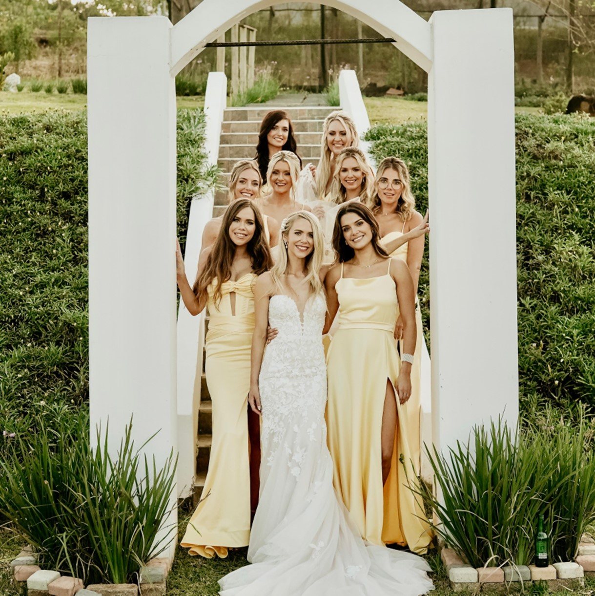 Bridal party with bride in white gown and bridesmaids in yellow dresses.