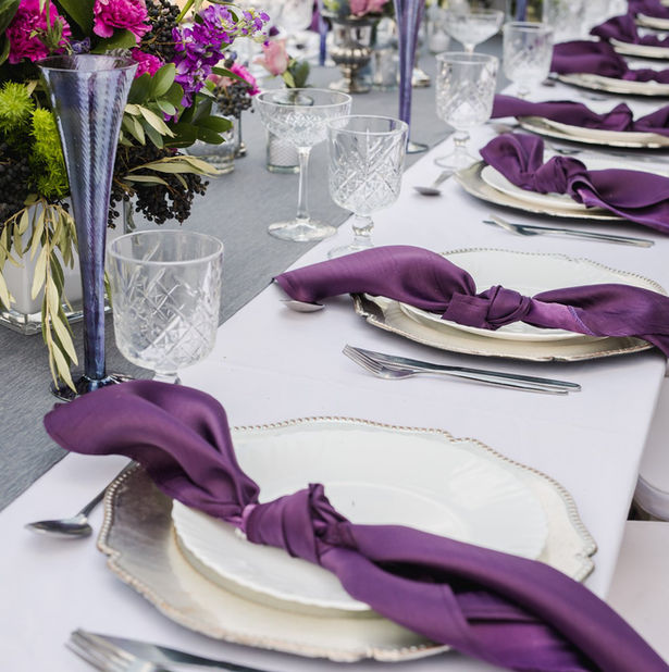 Table setting with white plates, crystal glasses, and purple napkins