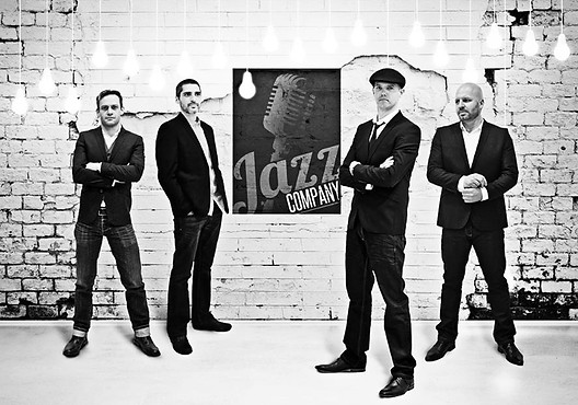 Black and white photo of a jazz band with a microphone backdrop.