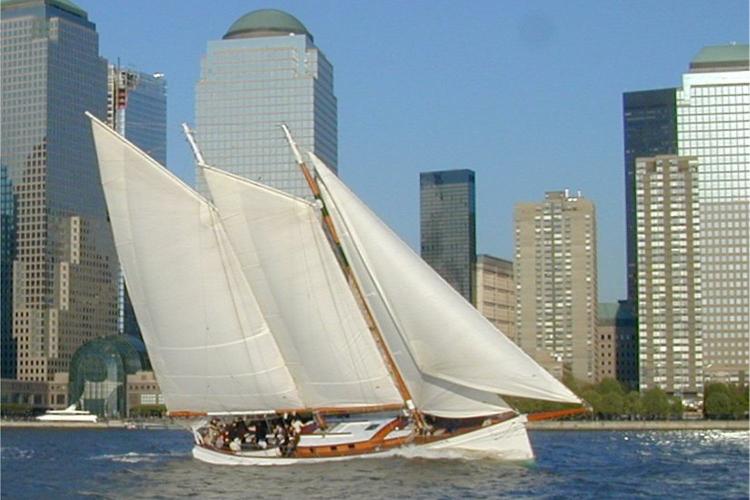 Sailboat with white sails sailing near a city skyline
