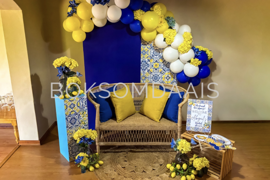 A cozy lounge setup with blue and yellow balloons and flowers.