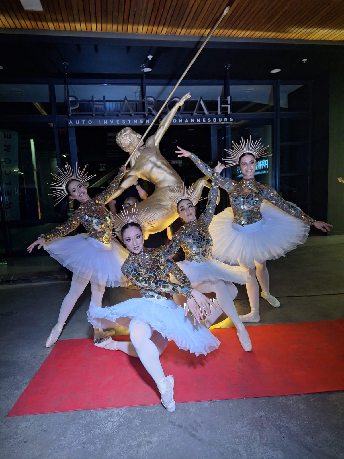 Four dancers in glittery costumes performing on a red carpet