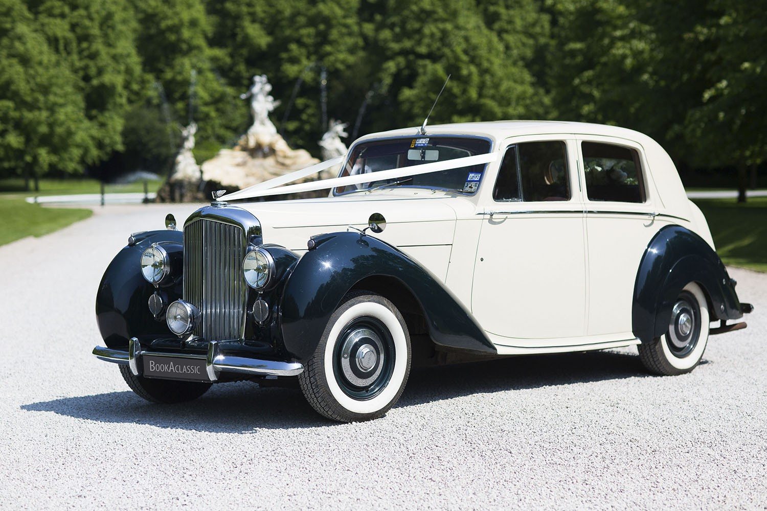 Vintage wedding car with white and black exterior parked on a gravel path