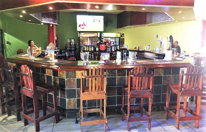 Wooden bar counter with high stools and a TV in the background.