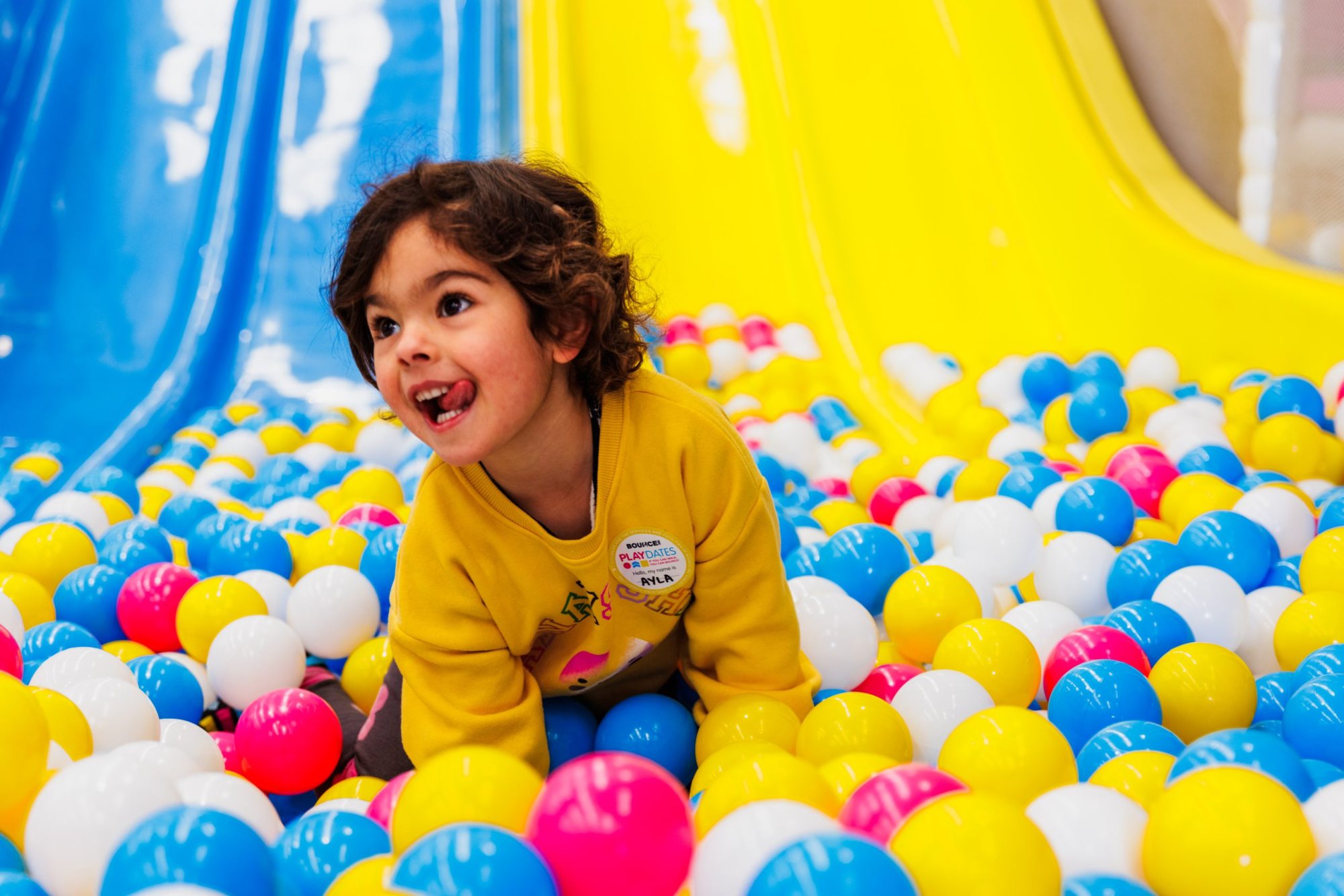 Child playing in a colorful ball pit with blue and yellow slides
