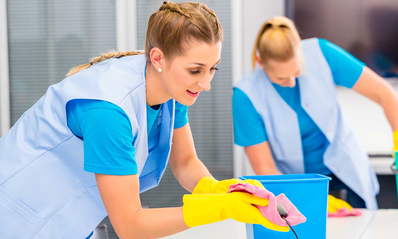Two women in blue cleaning a surface