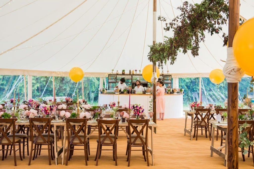 Interior of a tent featuring tables with flowers and a bar.