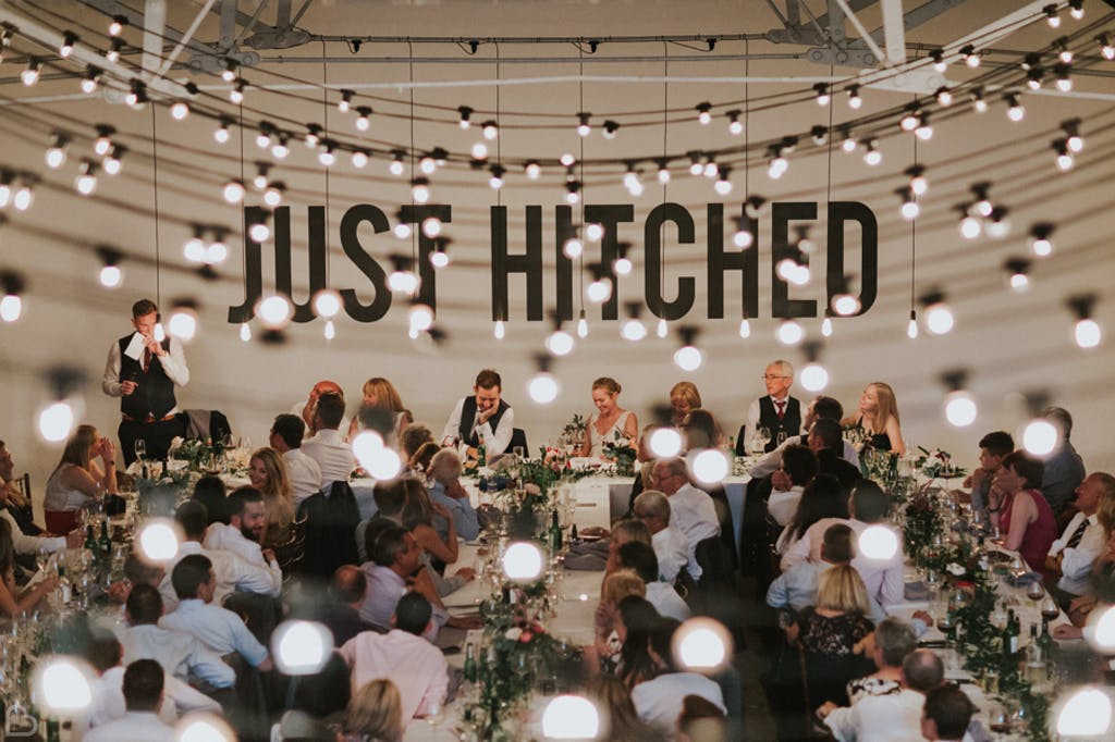 Wedding reception with guests dining and a 'JUST HITCHED' sign