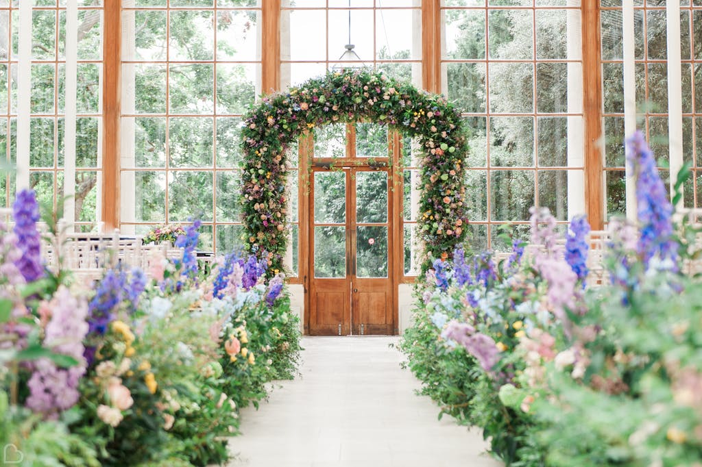 Floral arch with pink and purple flowers framing a wooden door.