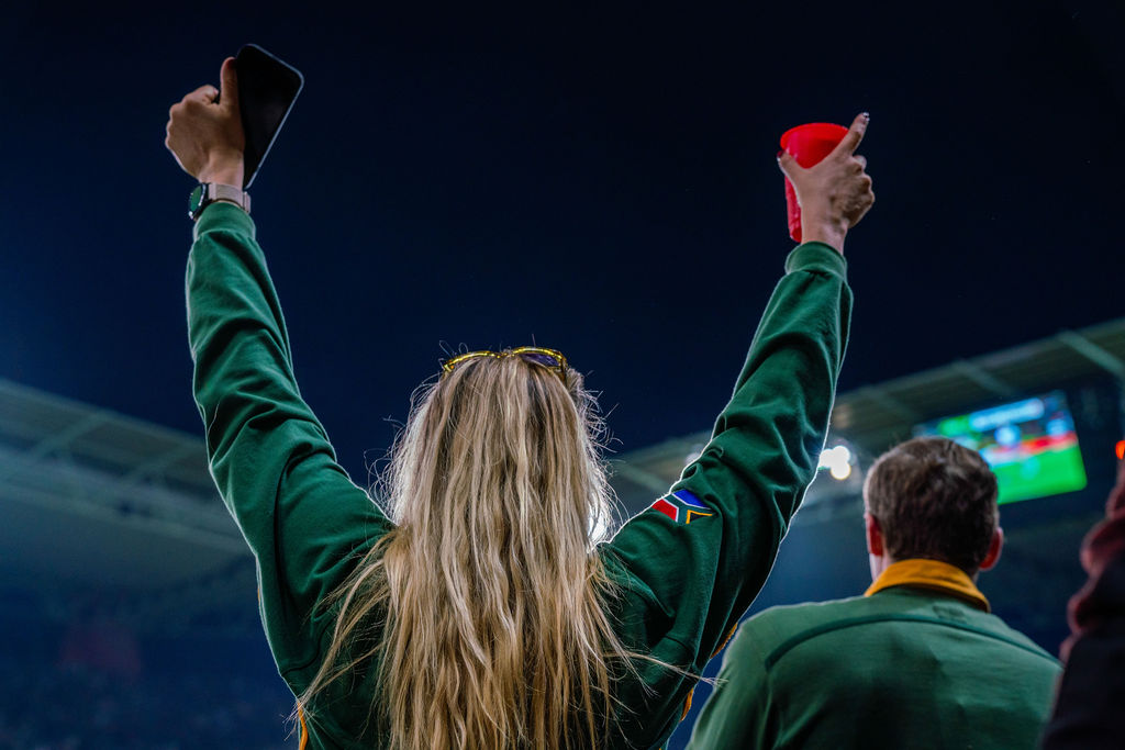Fan wearing a green jacket with South African flag celebrates.