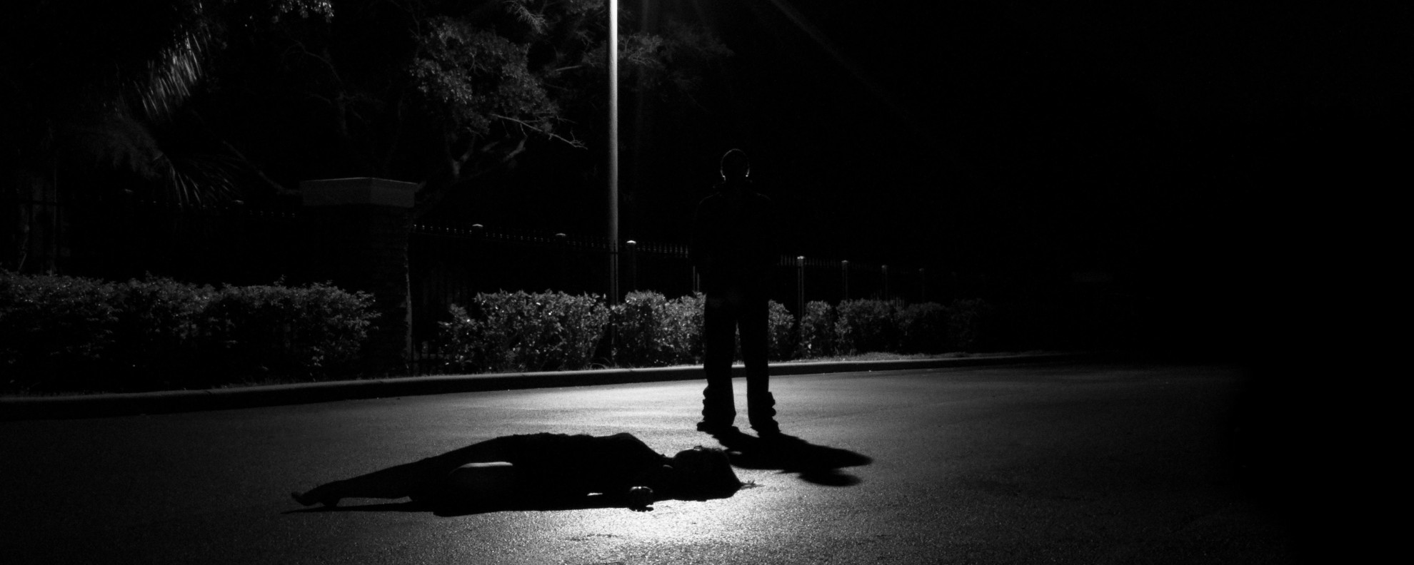 Black and white image depicting a crime scene with a figure and a body outline