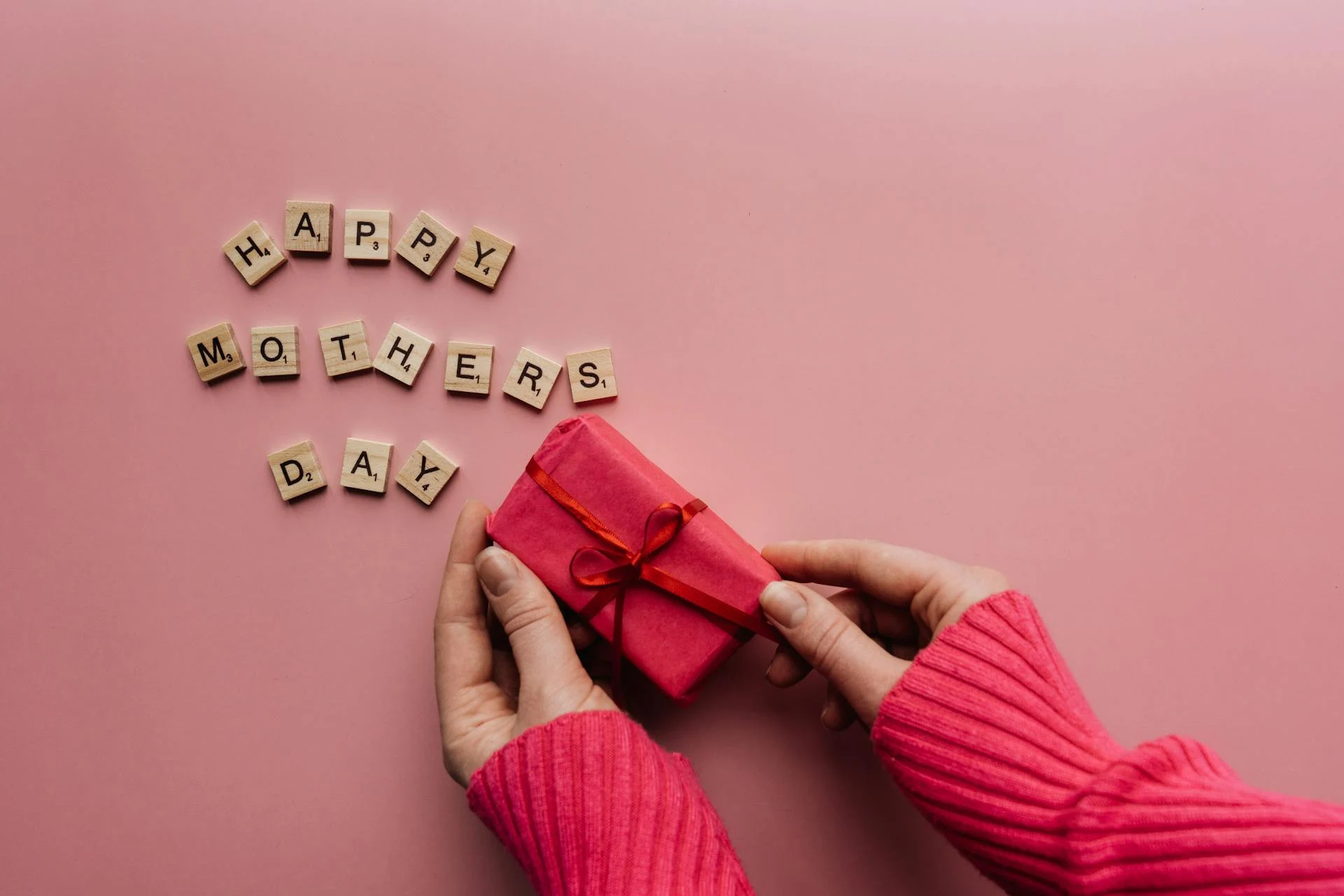A person holding a wrapped gift with blocks spelling Happy Mother's Day.