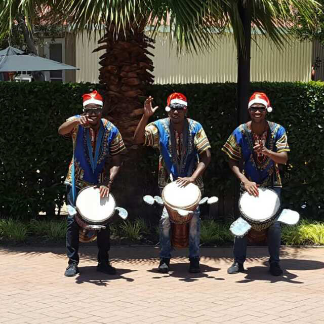 Three performers in traditional attire playing drums outdoors
