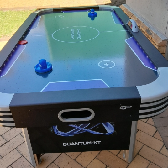 Air hockey table with blue paddles in an outdoor setting.