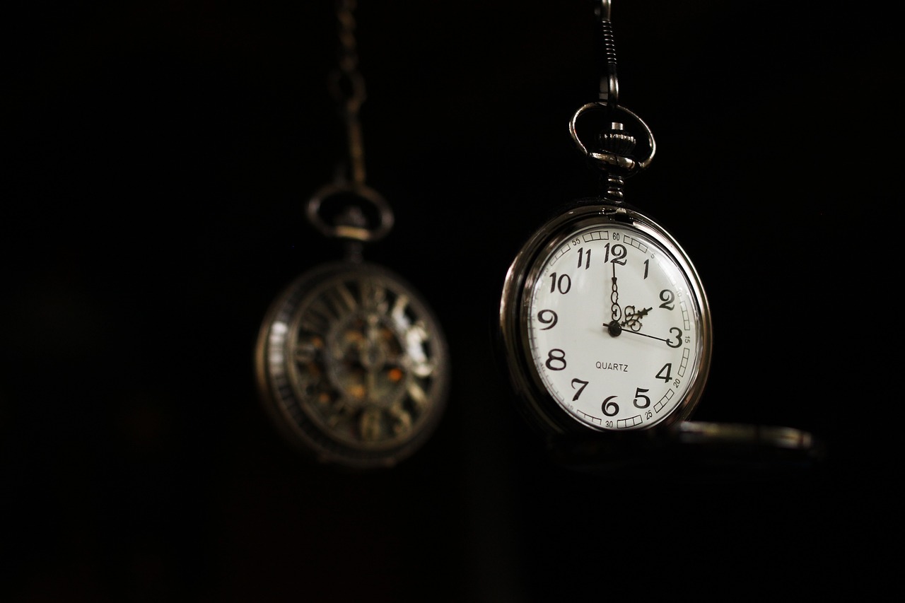 Two vintage pocket watches hanging against a dark background