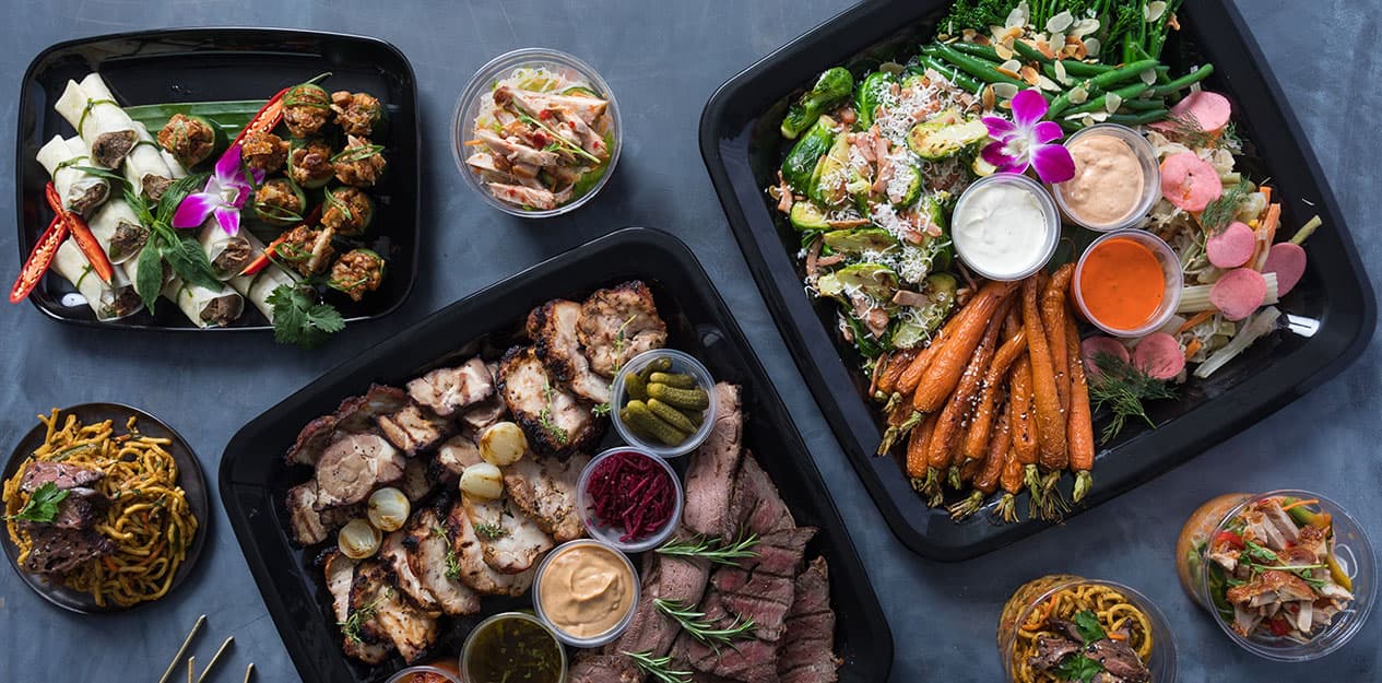 Assorted catering platters with meats, salads, and dips.