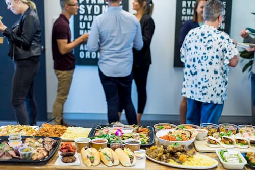 Catering spread with assorted dishes and attendees in background