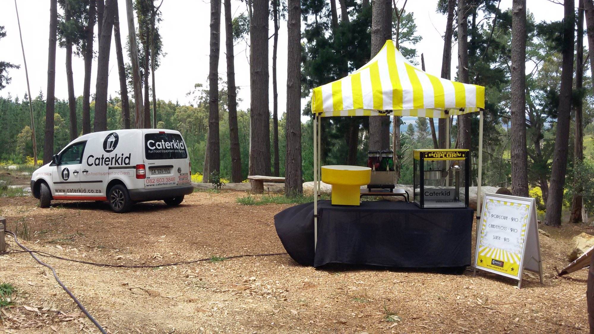 Popcorn machine setup under striped gazebo with Caterkid van