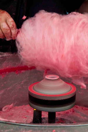 Hands preparing pink cotton candy in a machine.