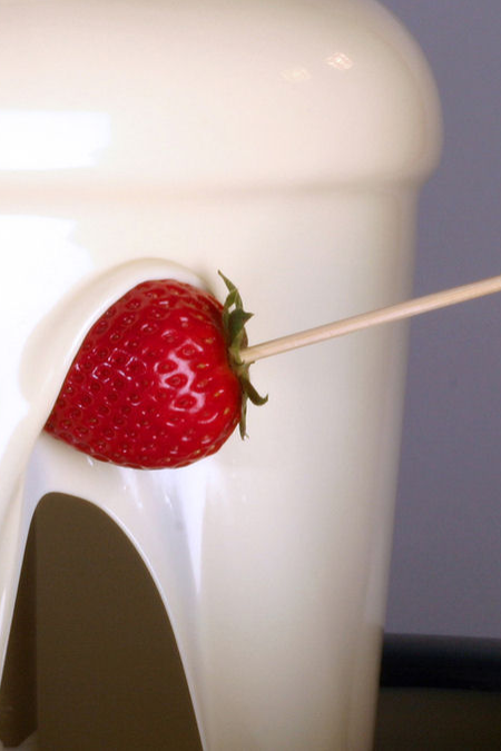 Strawberry on a stick next to a chocolate fountain.