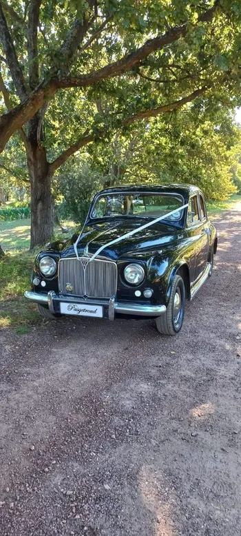 Black vintage car parked on a gravel path under trees.