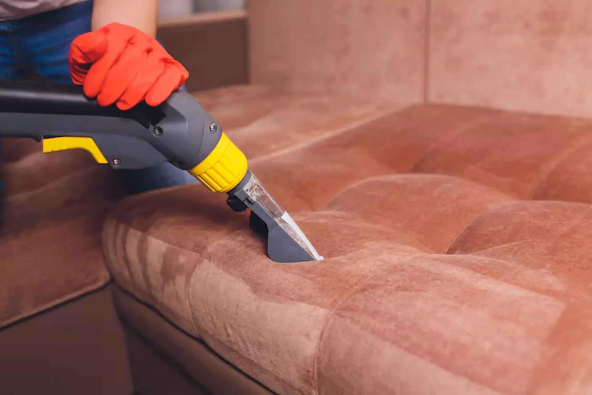 Person cleaning a brown couch with upholstery vacuum