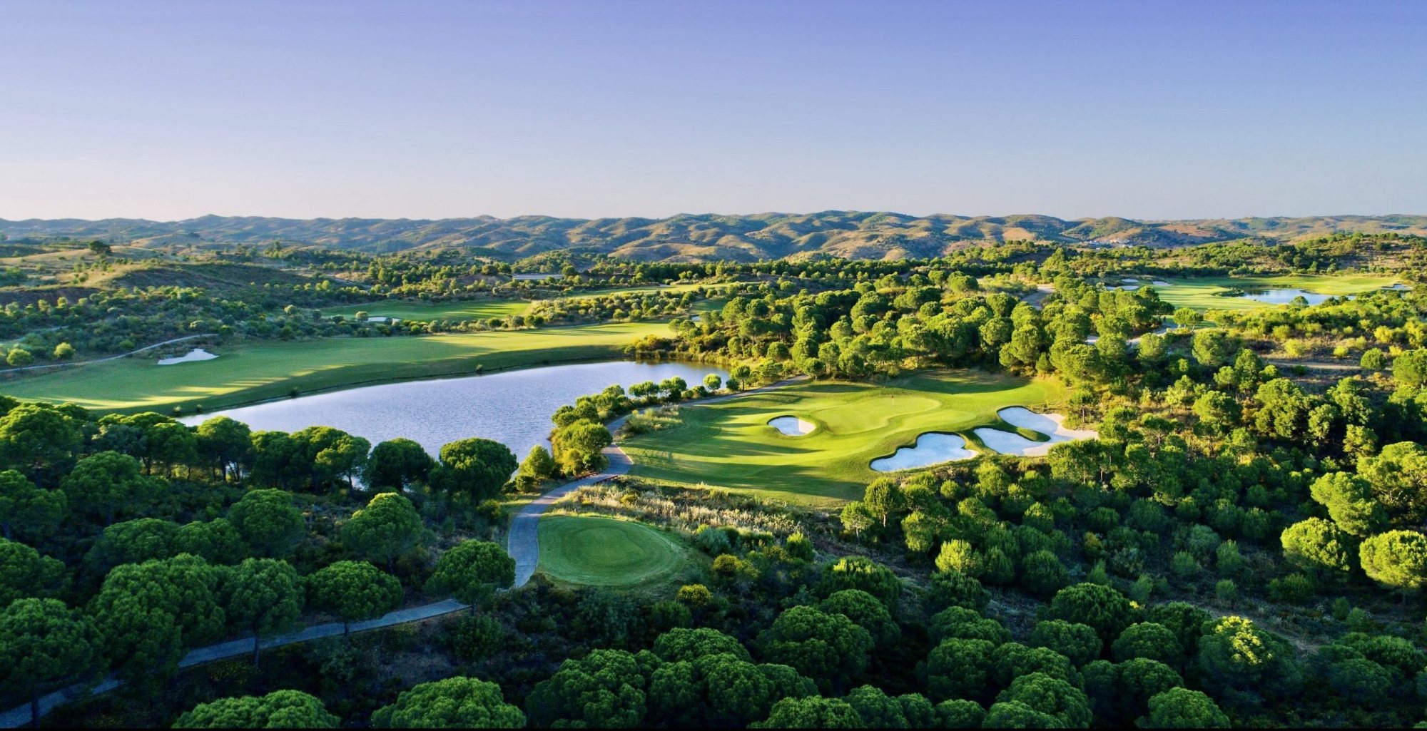 Aerial view of a golf course with hills and a lake.