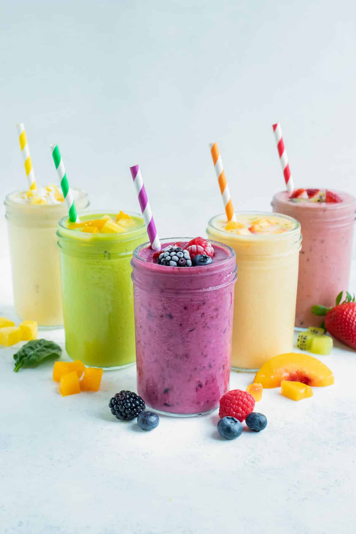 Five colorful fruit smoothies in jars with straws