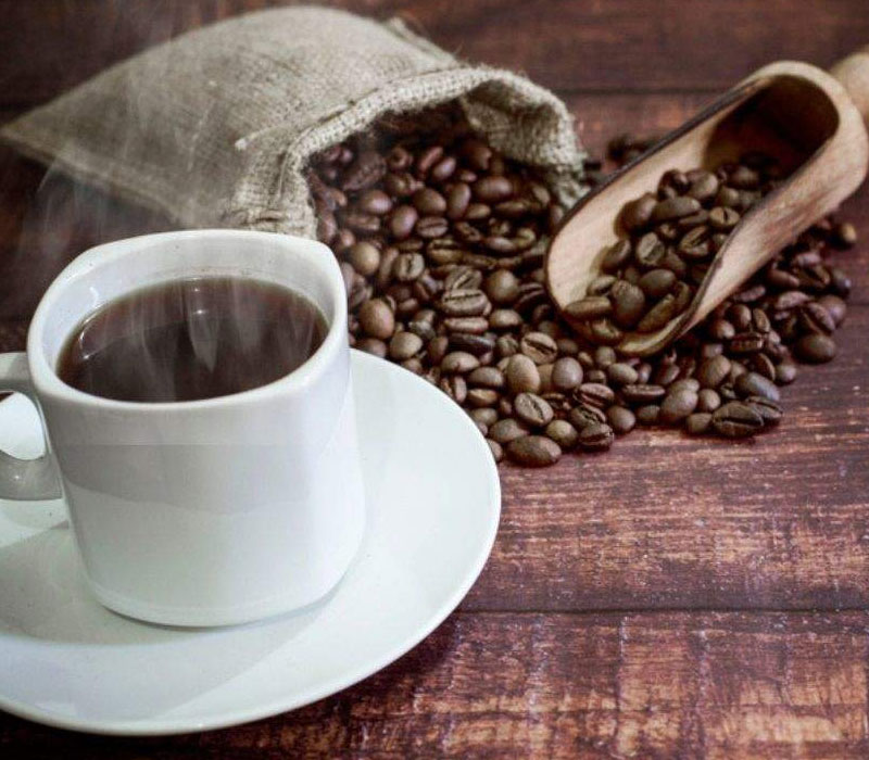 White cup of steaming coffee beside coffee beans